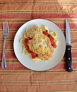 A plate of chicken parmesan over top of noodles.