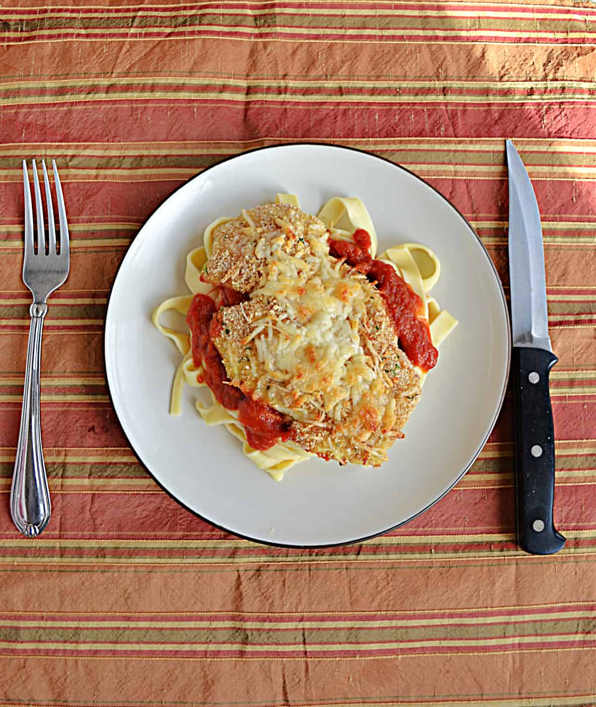 A plate of chicken parmesan over top of noodles. 
