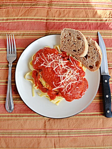 A plate of Chicken Parmesan with 2 pieces of bread on the plate and a knife and fork next to the plate.
