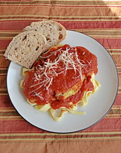 A plate of Chicken Parmesan with a piece of bread on the plate.