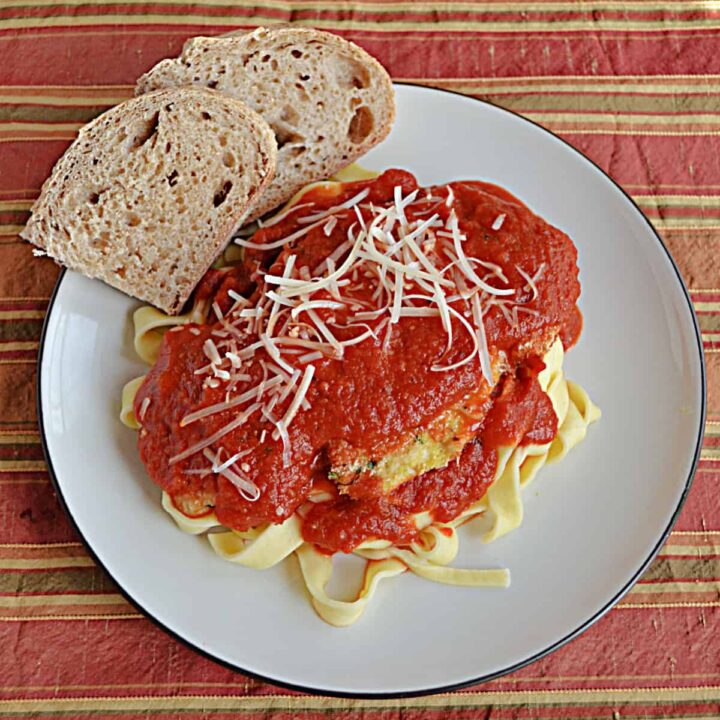 A plate of Chicken Parmesan with a piece of bread on the plate.