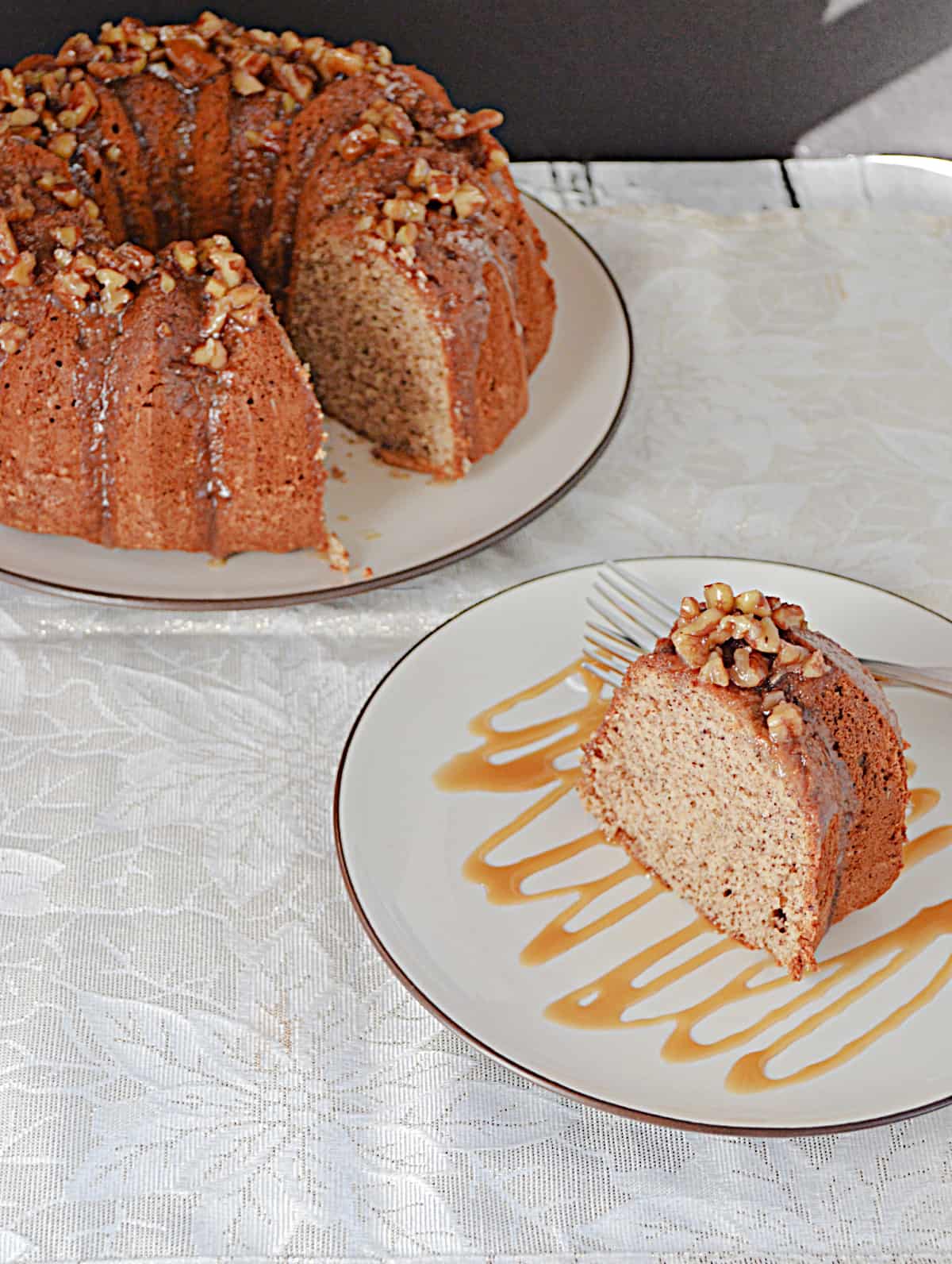 A close up of a slice of pecan cake drizzled with caramel and the whole Bundt cake before it. 