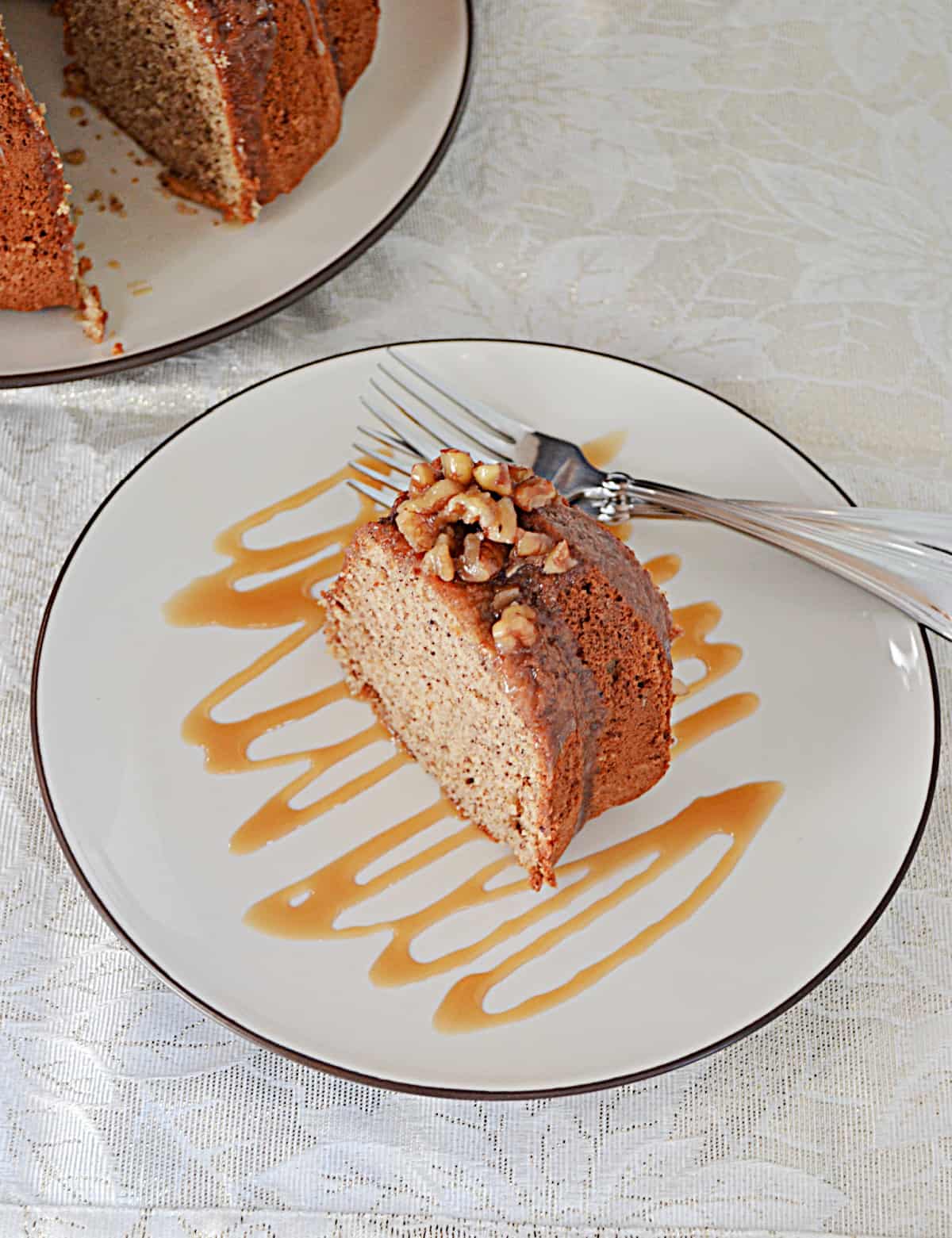 A slice of pecan cake drizzled with caramel sauce and a fork on the plate.