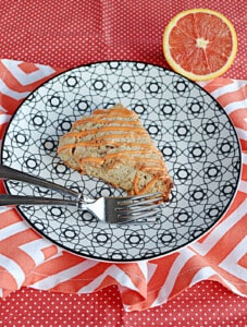 A plate with a scones drizzled with glaze and an orange in the background.
