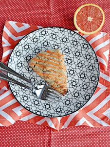 A plate with a scones drizzled with glaze, 2 forks on the plate, and an orange in the background.