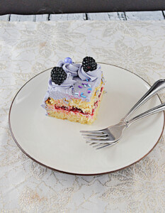 A slice of cake on a plate with 2 forks on the plate.