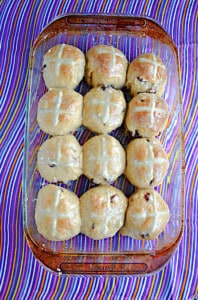A pan of hot cross buns with glaze and a white cross on top.