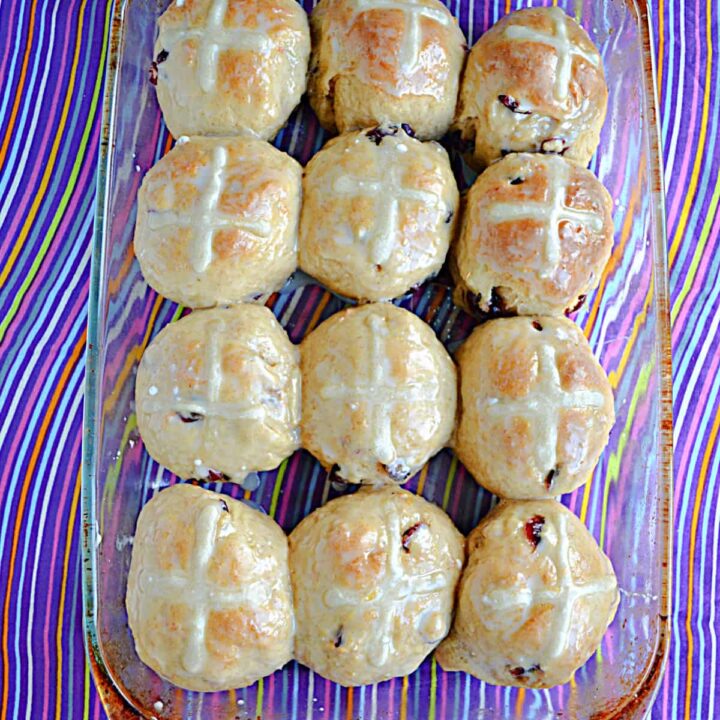 A pan of hot cross buns with glaze and a white cross on top.