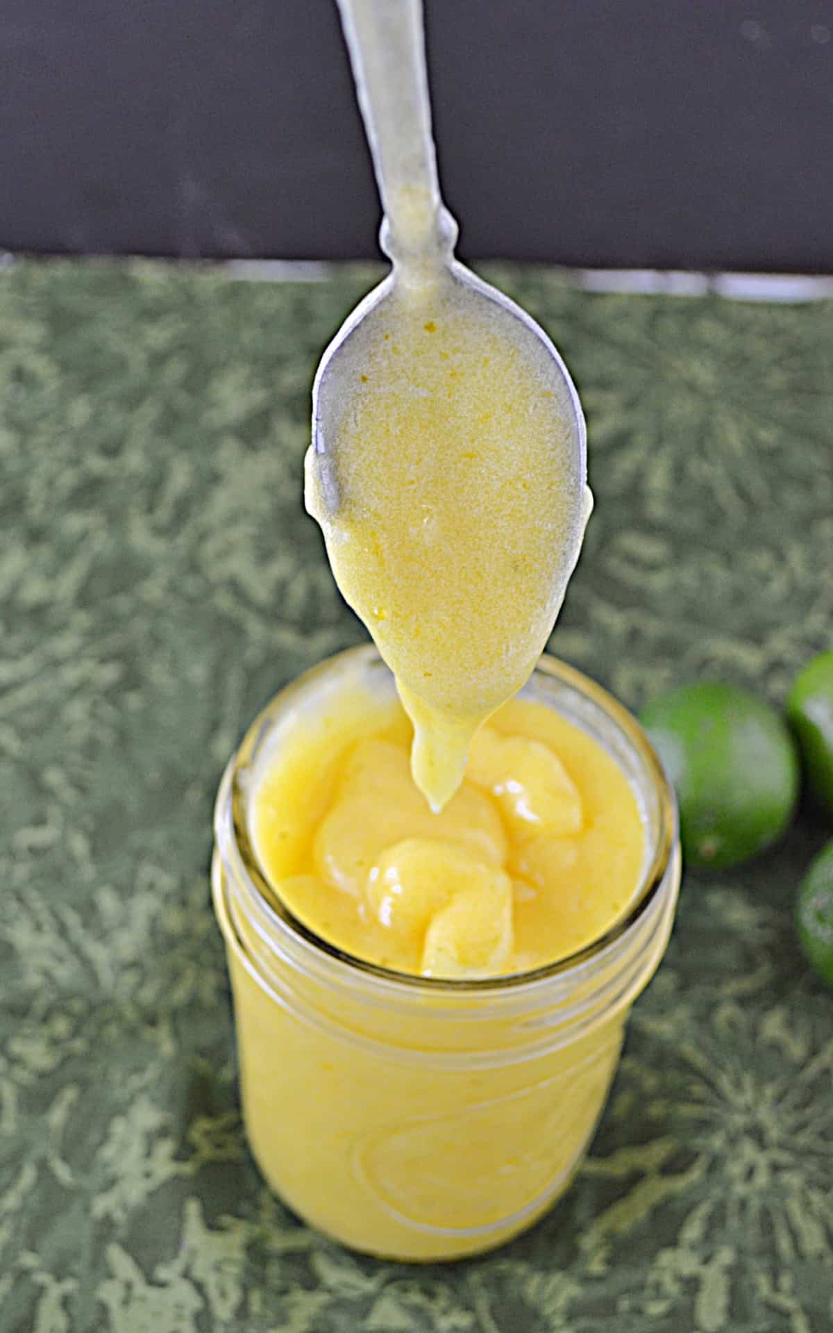 A close up of a jar of key lime curd with a spoonful of key lime curd. 