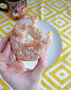 A close up of a hand holding a donut with a bite taken out of it.
