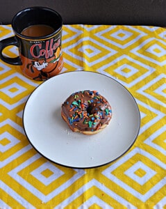 A plate with a chocolate glaze donut and a coffee mug.