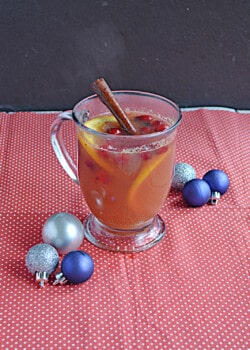 A mug of cider with a cinnamon stick in it and silver and blue ornaments around it.