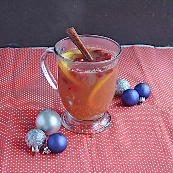 A mug of cider with a cinnamon stick in it and silver and blue ornaments around it.