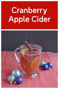 Pin Image: Text title, a mug of cider with a cinnamon stick and orange slices with blue and silver ornaments around it.