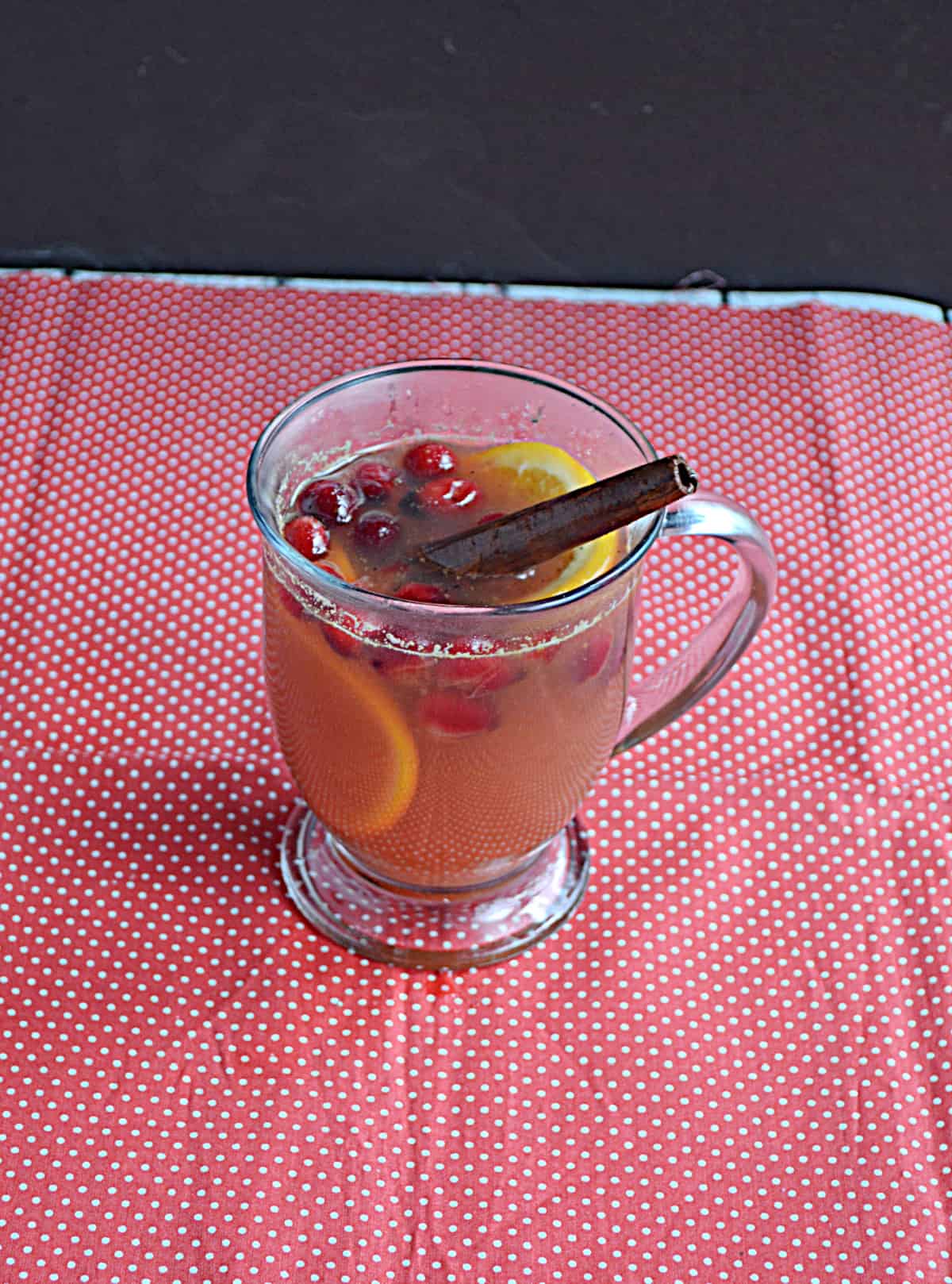 A mug of cider with cinnamon sticks, cranberries, and oranges in it.