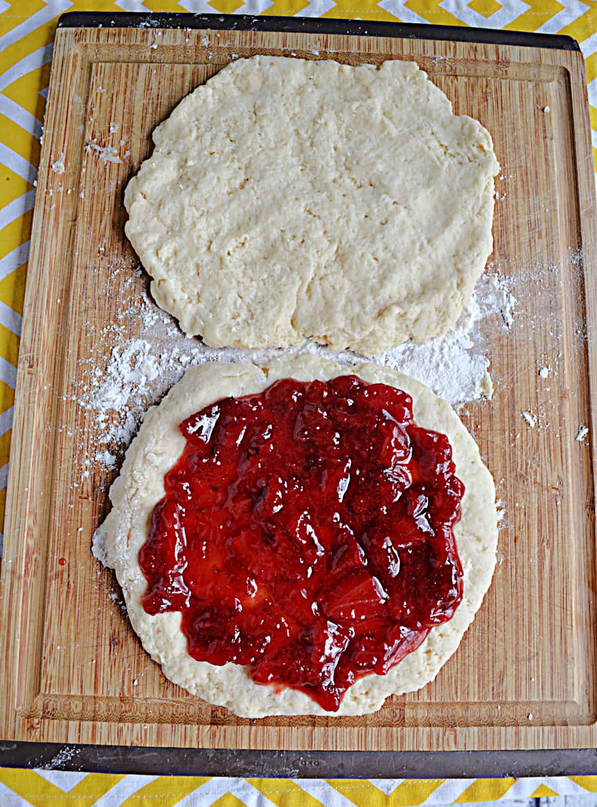 Two rounds of scone dough, one with strawberry jam on top. 