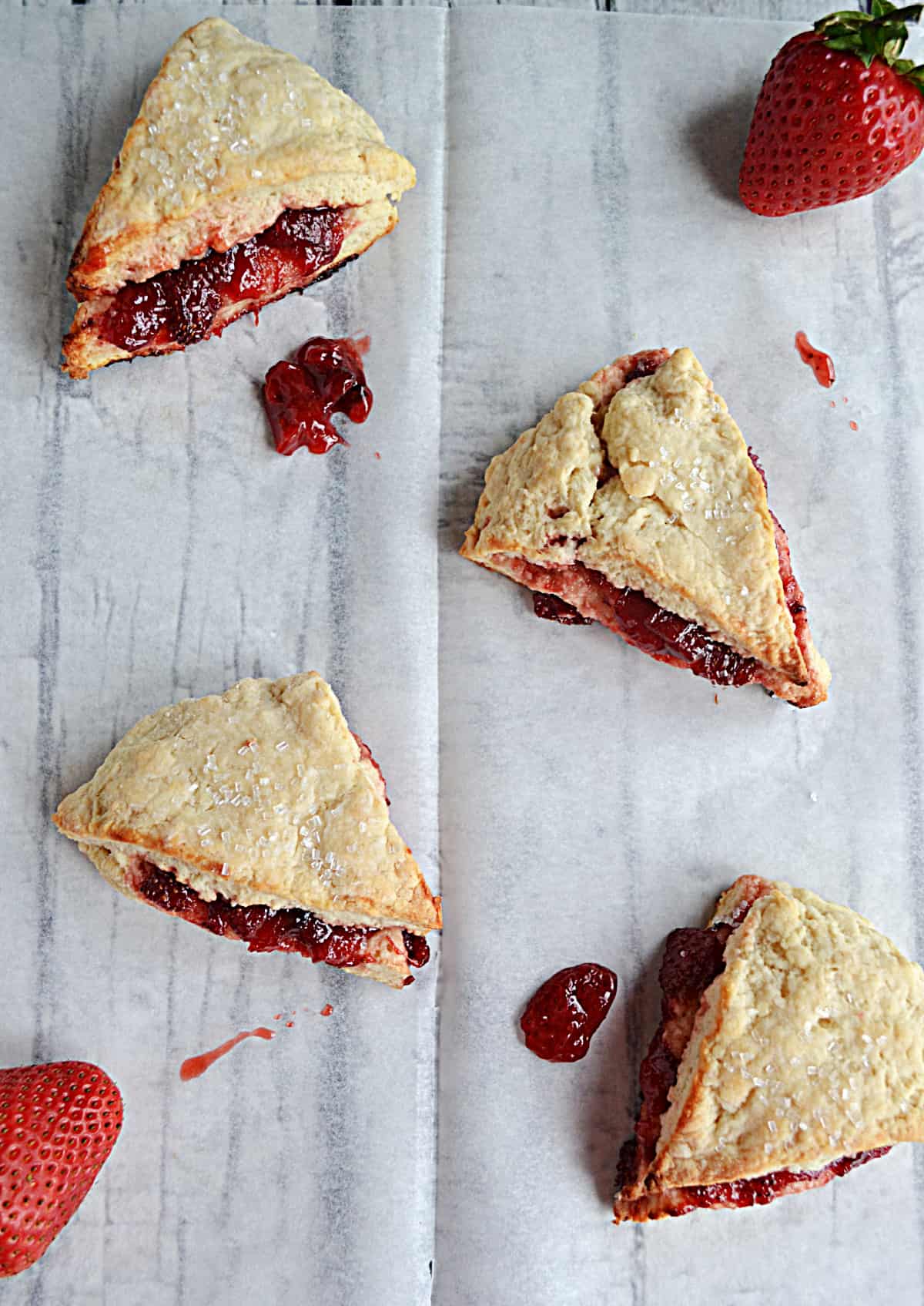 Four scones with strawberry jam falling out of each one.
