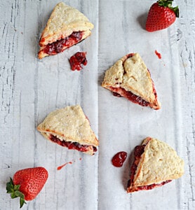Several scones with strawberry jam coming out of each one along with fresh strawberries.