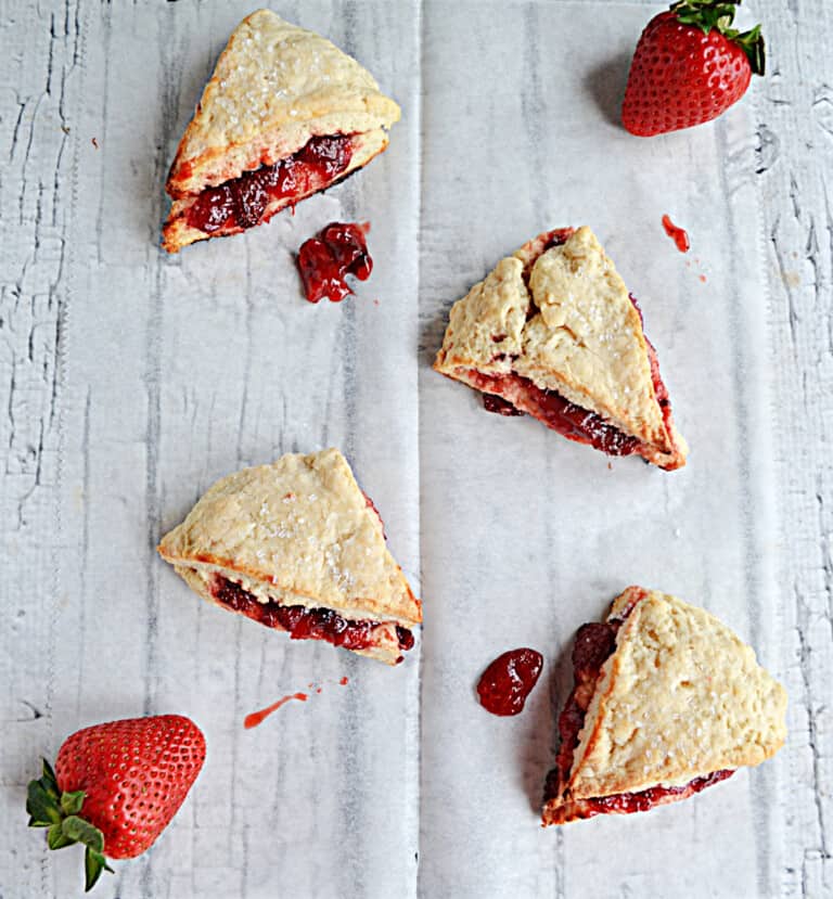 Several scones with strawberry jam coming out of each one along with fresh strawberries.