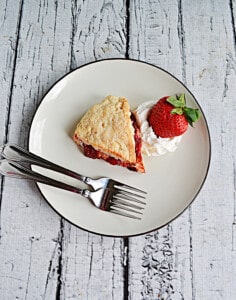 A scone with whipped cream and a strawberry on the side along with 2 forks.