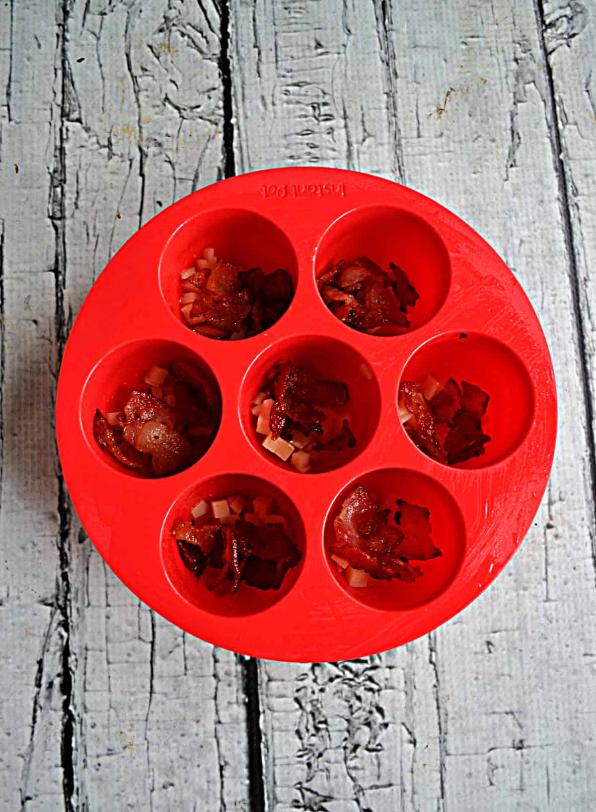Silicone egg bite mold with bacon in the cups.