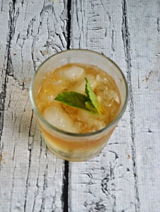 A top view of a glass with bourbon over ice and a mint leaf.