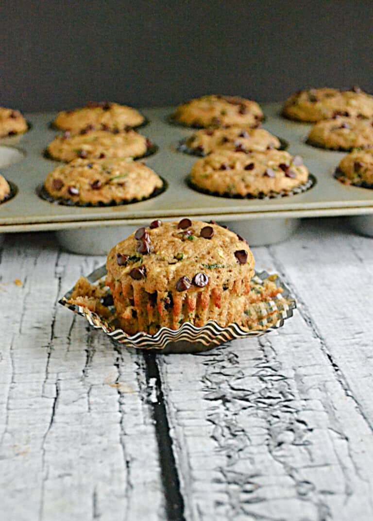 A Chocolate Chip Zucchini Muffin sitting in front of a pan of zucchini muffins.