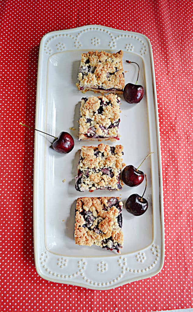 A platter with four cherry crumble bars and fresh cherries on it.