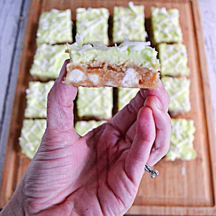 A hand holding a coconut lime bar with a bite out of it.