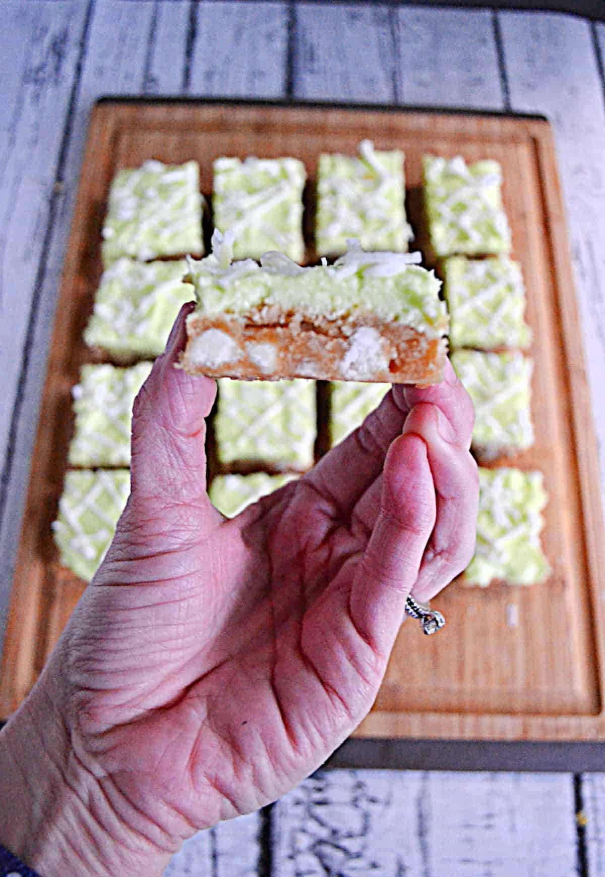 A hand holding a coconut lime bar with a bite out of it.