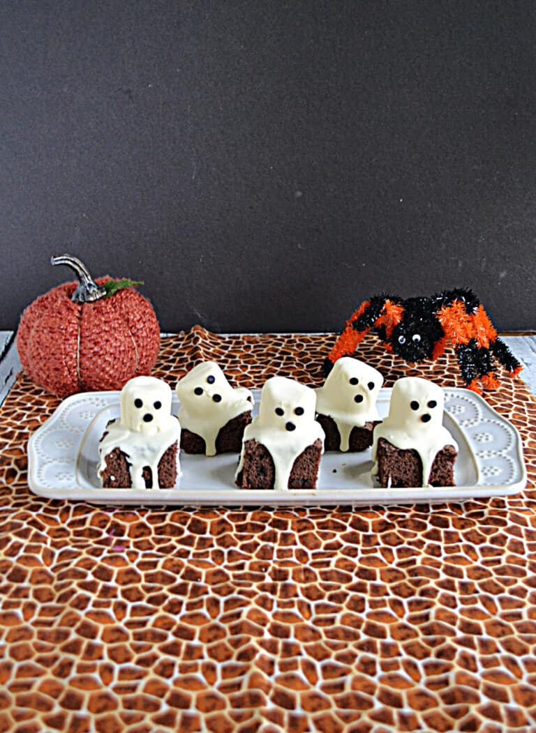 A platter with ghost brownies on it and a pumpkin and spider behind the platter.