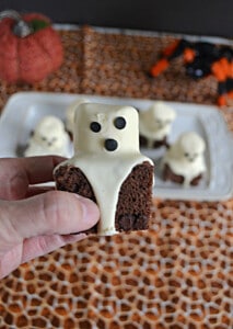 A close up of a hand holding a brownies with a ghost marshmallow on top of it.