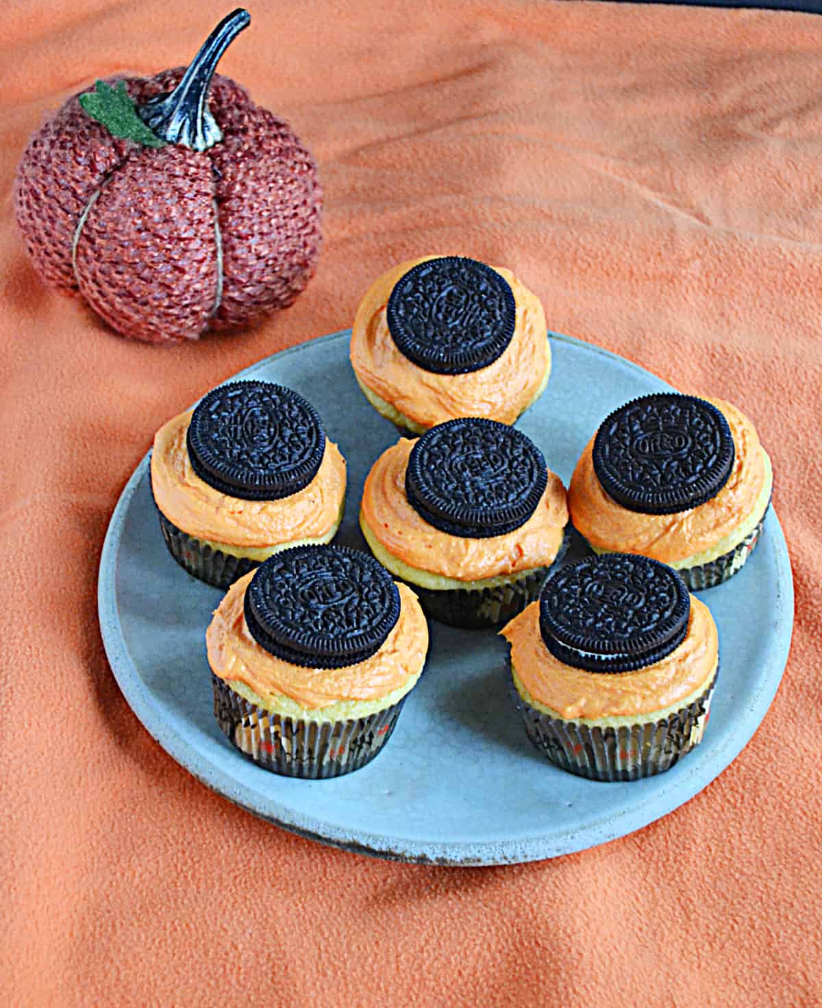 A plate with cupcakes, orange frosting, and Oreos on top with a pumpkin in the background.