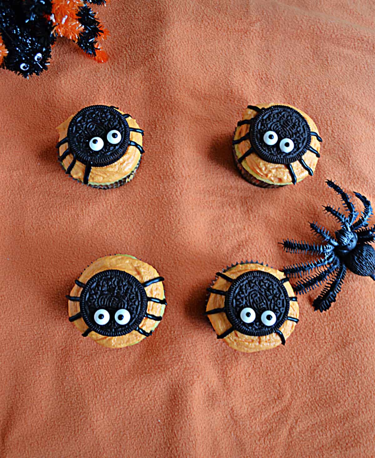 Four cupcakes with Oreo spiders on top and two toy spiders in the background.