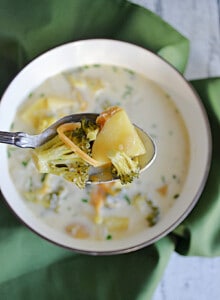 A spoonful of Broccoli Cheddar Soup with a bowl of the soup behind it.