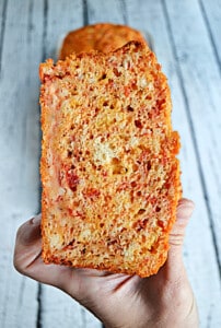 A close up view of a hand holding a piece of Tomato Bread.