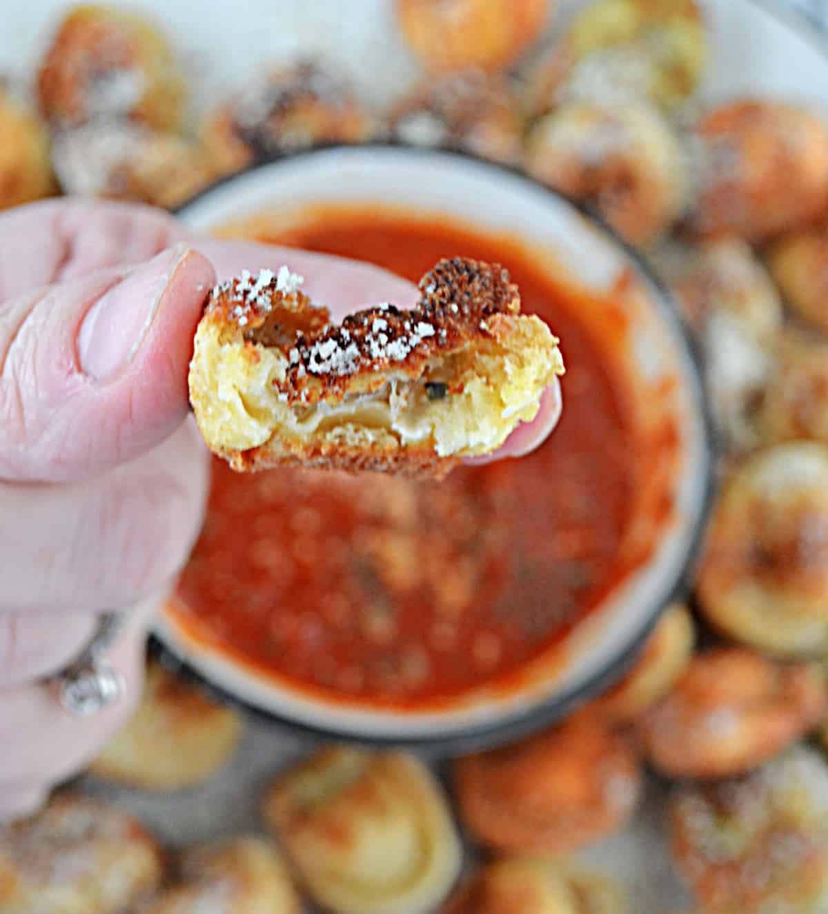 A hand holding a fried tortellini that has a bite taken out of it.