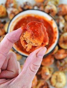 A hand holding a fried tortellini with sauce on it.
