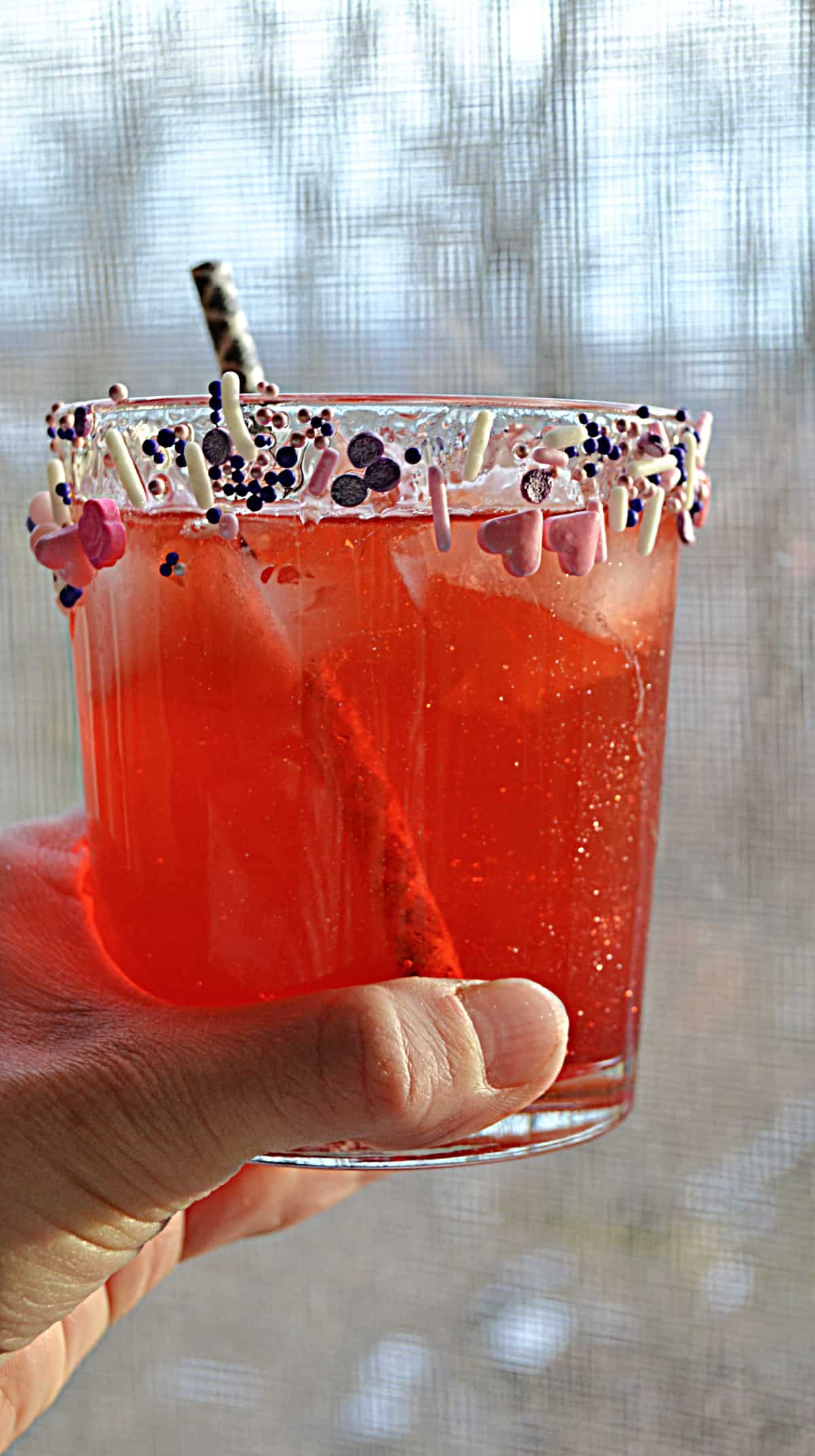 A close up view of a hand holding a berry mocktail with a straw in the glass.