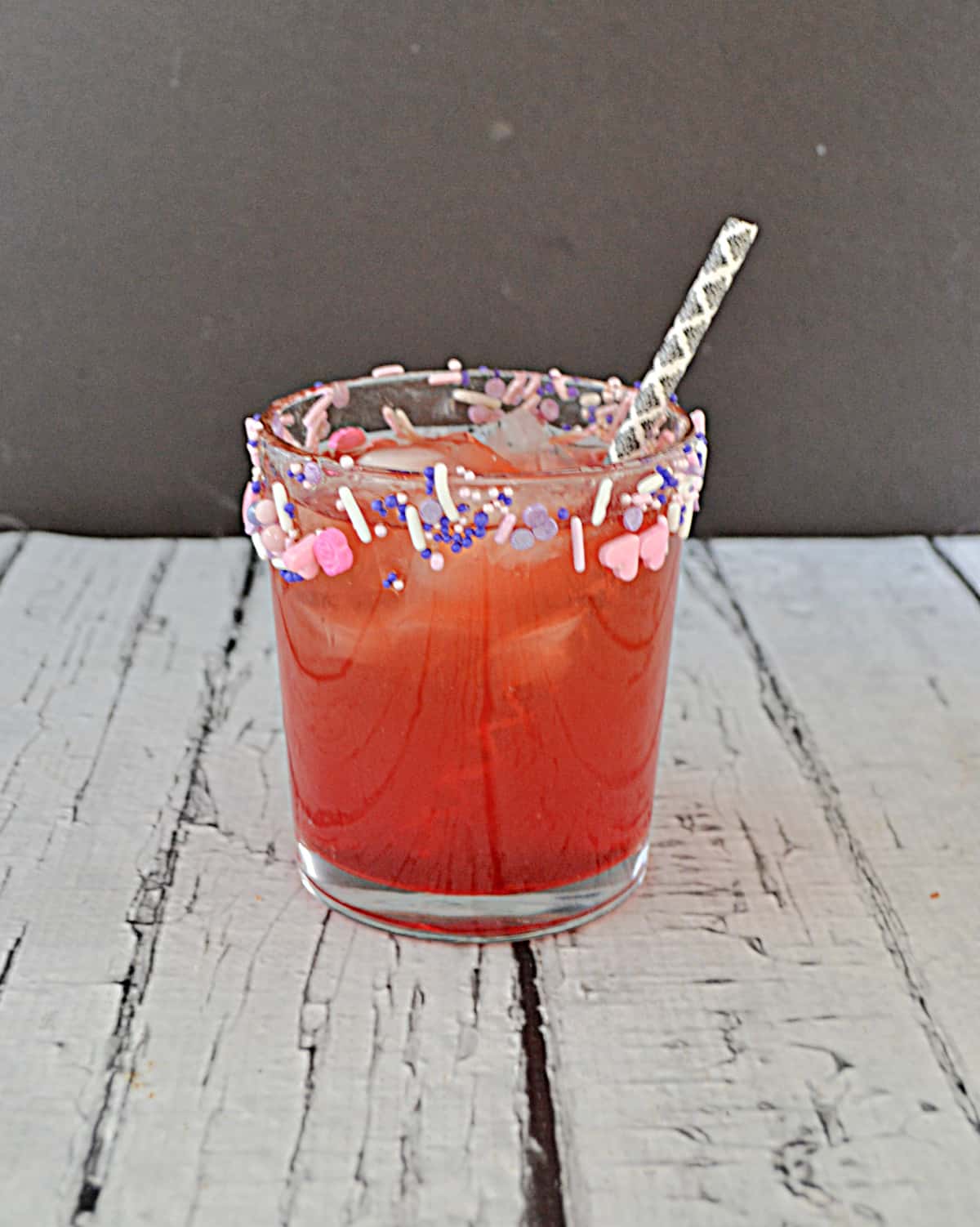 A glass of berry mocktail with sprinkles around the rim.