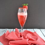 A champagne glass of strawberry cocktail with a strawberry on the rim.
