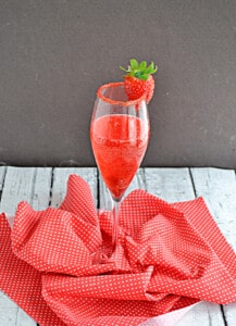 A champagne glass of vodka champagne cocktail with red sugar rim and strawberry on the rim.