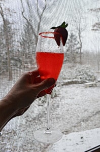 A hand holding a glass of champagne cocktail with strawberries.