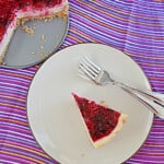 A slice of cheesecake with dragon fruit jam on top and the whole cheesecake behind the piece.