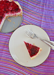 A slice of cheesecake with dragon fruit jam on top and the whole cheesecake behind the piece.