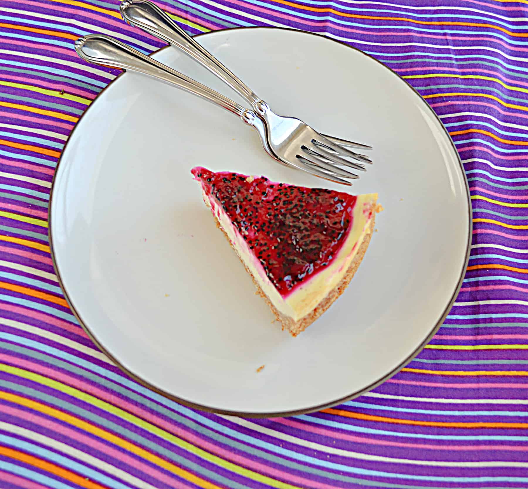 A slice of cheesecake with dragon fruit jam on a plate with 2 forks.