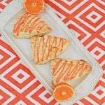 A platter with three scones drizzled with tangerine glaze and a tangerine cut in half.