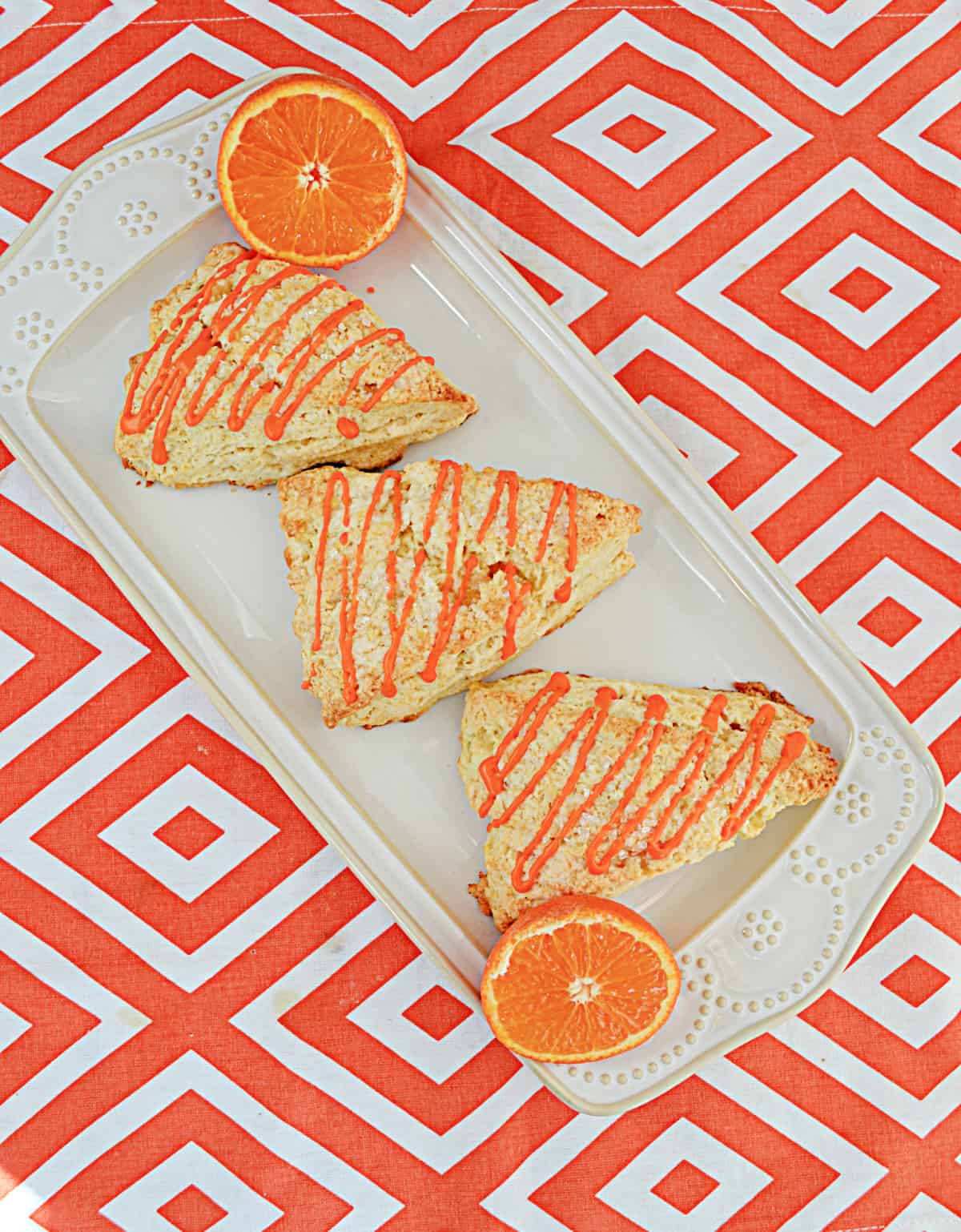 A platter with three scones drizzled with tangerine glaze and a tangerine cut in half.