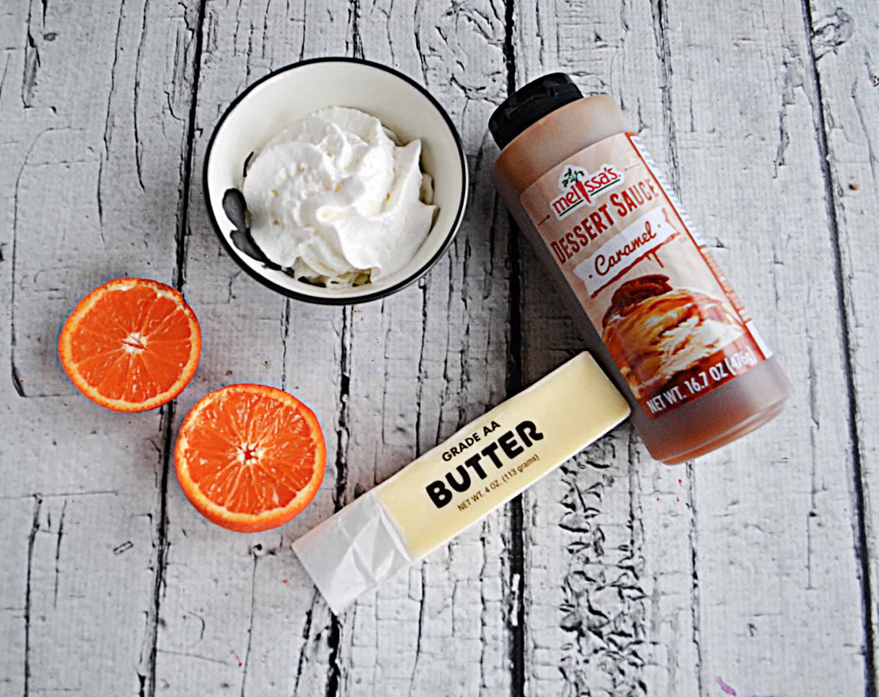 A bottle of caramel sauce, whipped cream, a tangerine, and a stick of butter.
