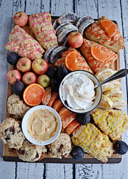 A board covered with fruit, scones, and spreads.